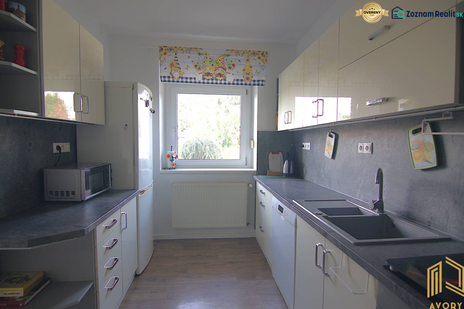 Családi ház konyhája fehér szekrényekkel, nagy ablakkal és háztartási gépekkel.