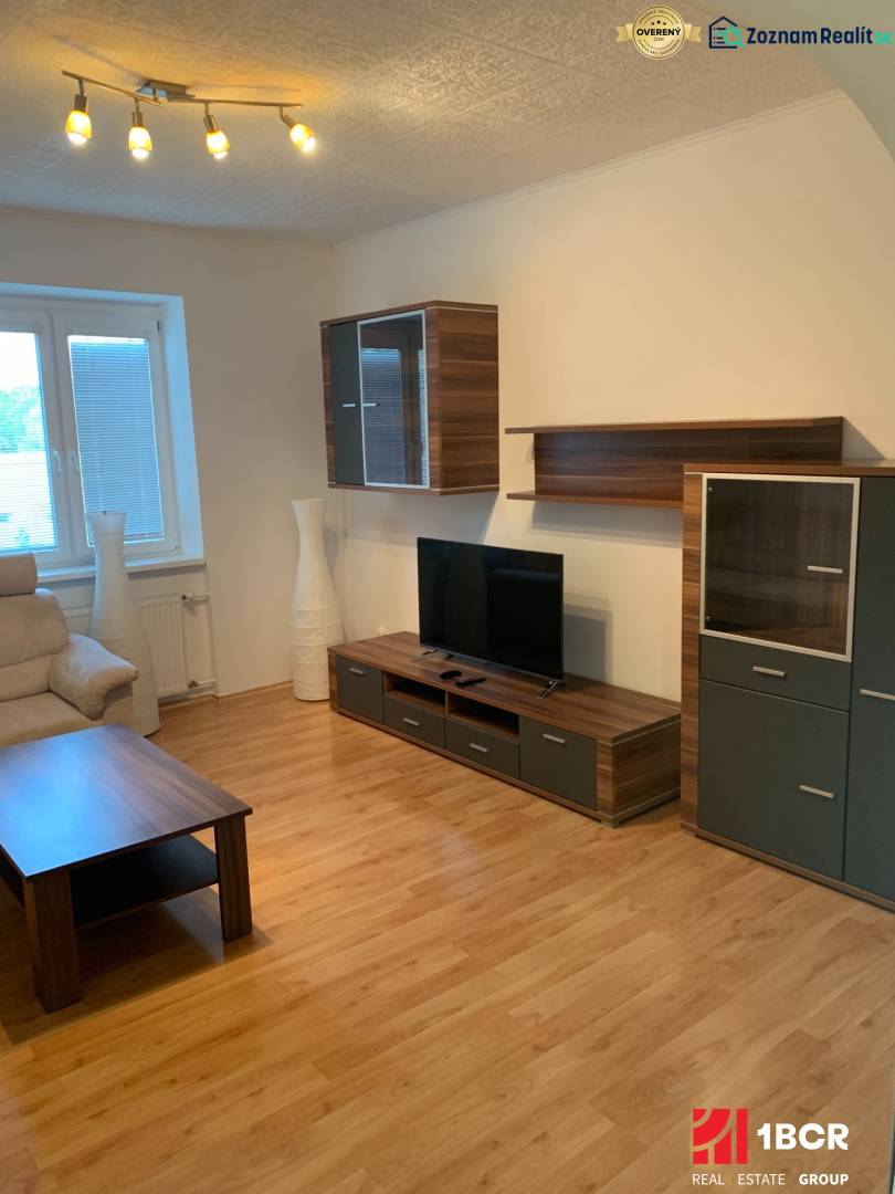 Nappali egy kétszobás lakásban fa dekor padlóval és televízióval.