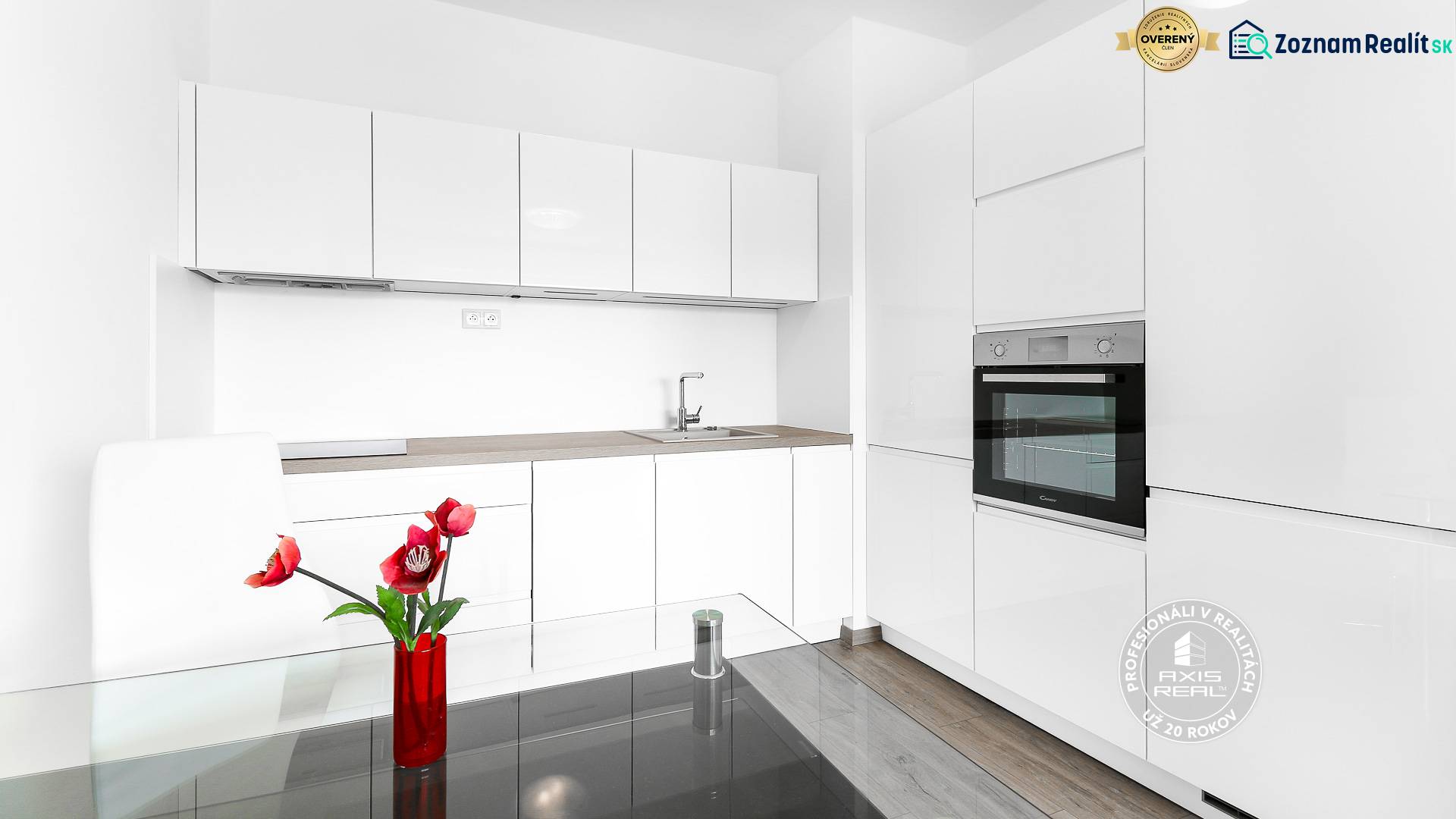 Konyha fehér szekrényekkel egy kétszobás lakásban, fa dekor padló, piros virágok.