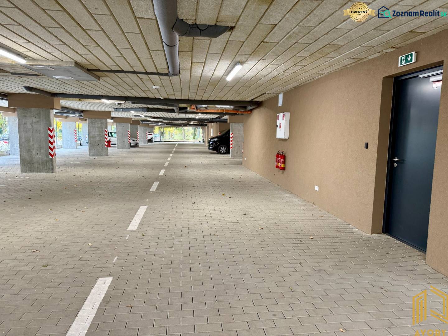 Parkolóhelyekkel és jelzésekkel ellátott parkoló, burkolata térkő, a garázsokban.