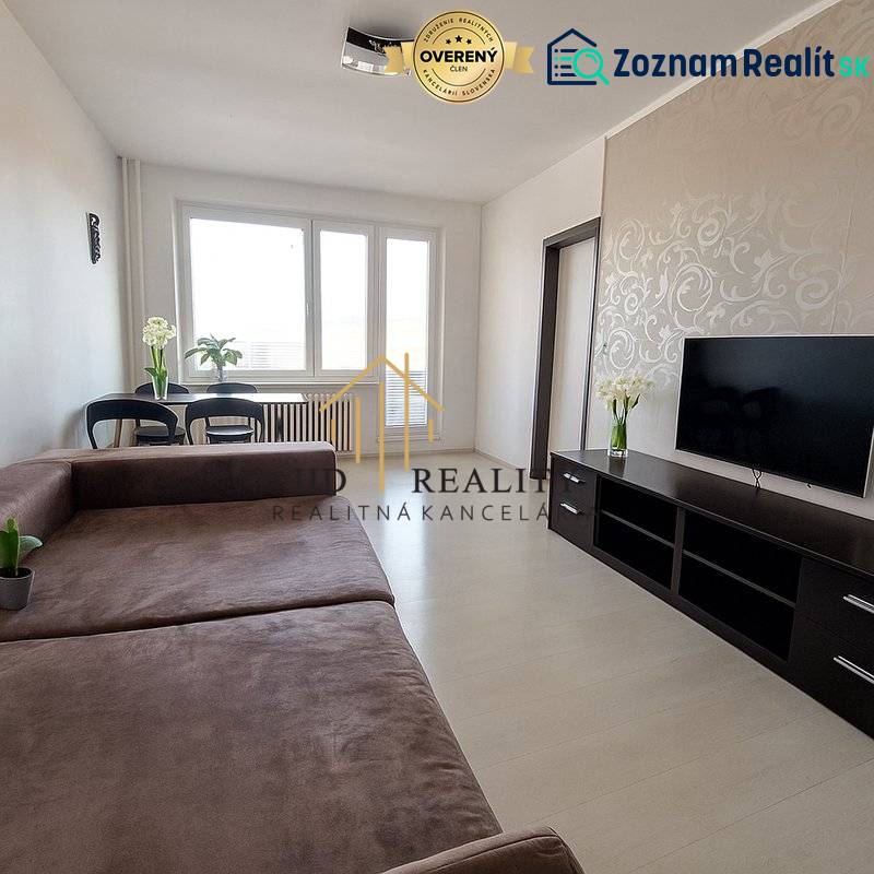 Nappali egy háromszobás lakásban nagy kanapéval, TV-vel és fa mintázatú padlóval.