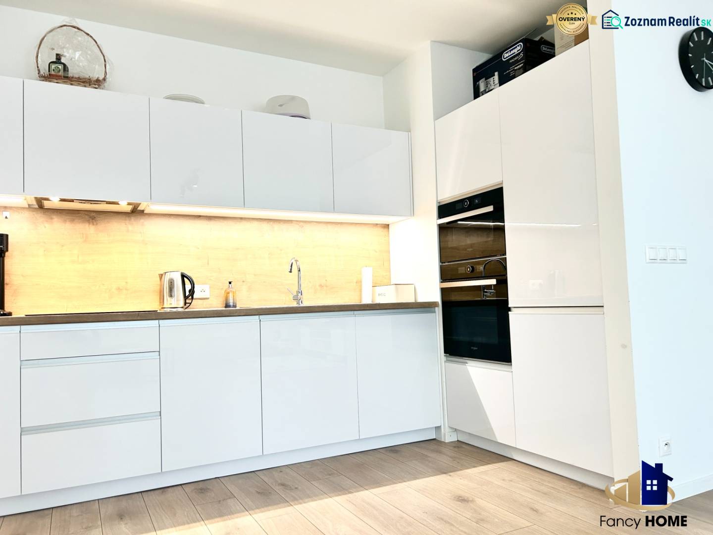 Konyha egy kétszobás lakásban fehér szekrényekkel és fa mintázatú padlóval.