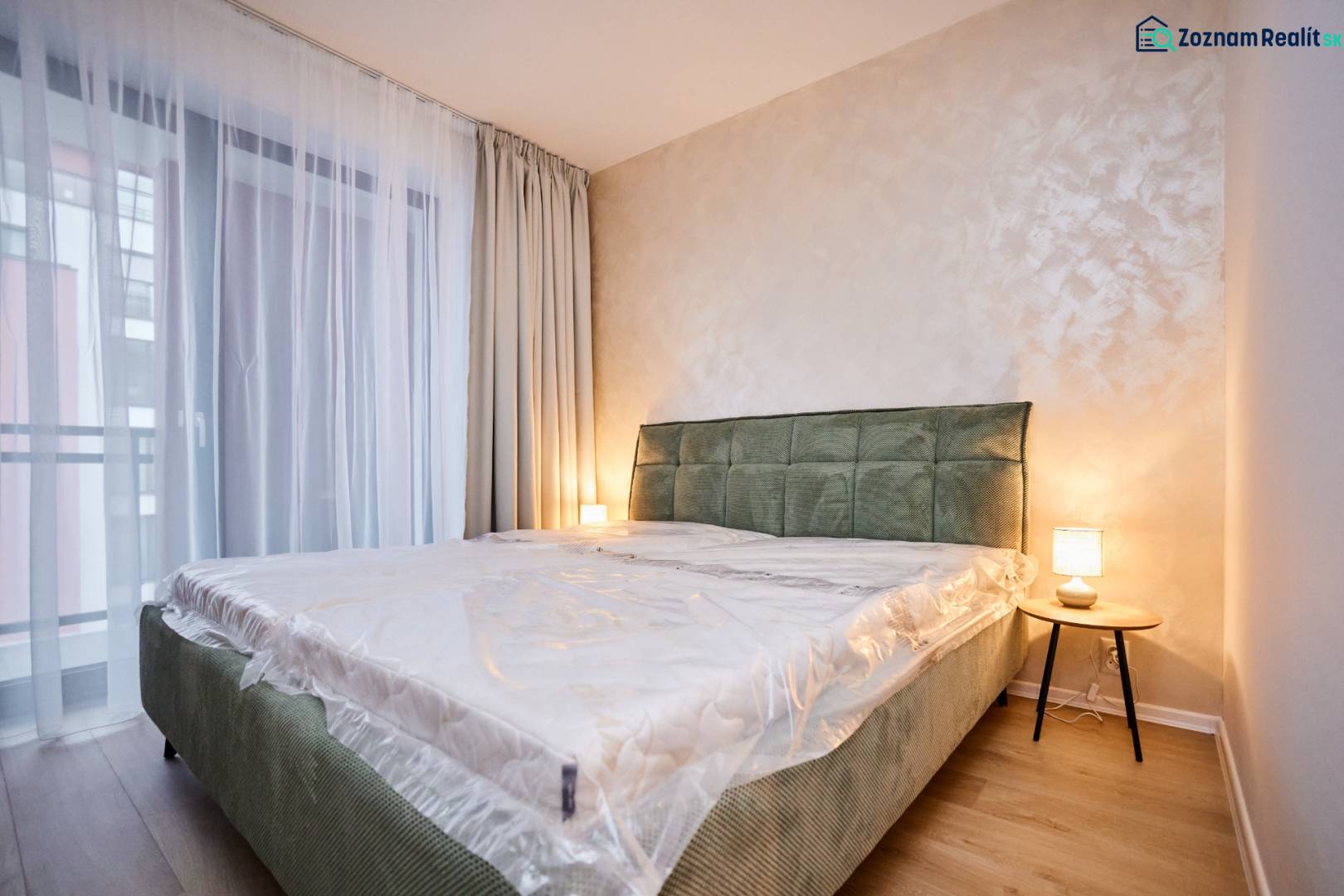 Hálószoba egy kétszobás lakásban ággyal, lámpával és fa dekorációjú padlóval.