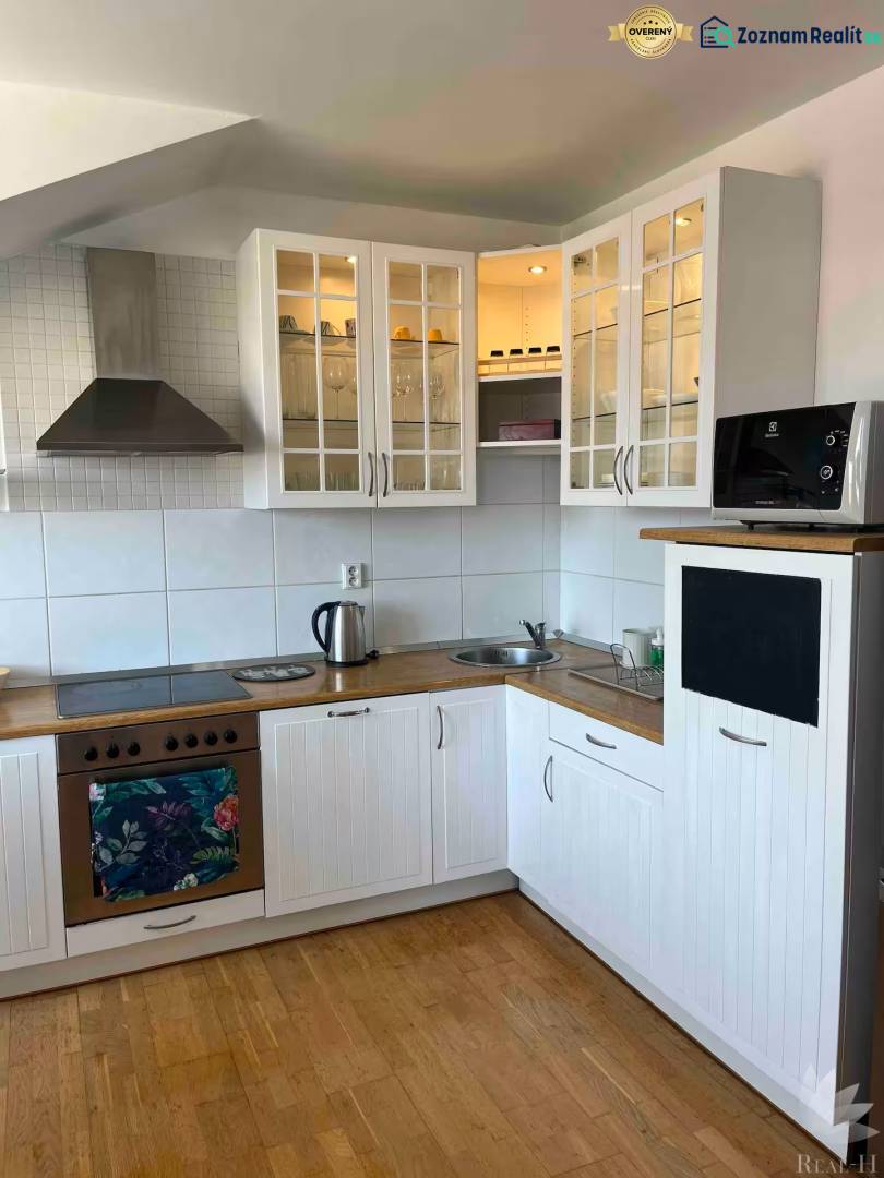 Konyha egy háromszobás lakásban fa padlóval, fehér szekrényekkel és tárolóhellyel.