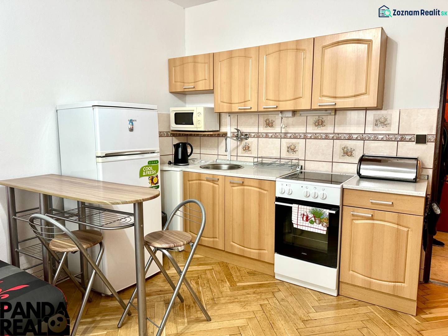 Konyha garzonlakásban fa mintázatú padlóval, háztartási gépekkel és ülőhellyel.