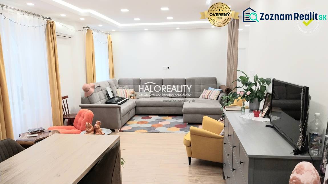 Nappali egy háromszobás lakásban fa dekor padlóval, szürke kanapéval és sárga fotellel.