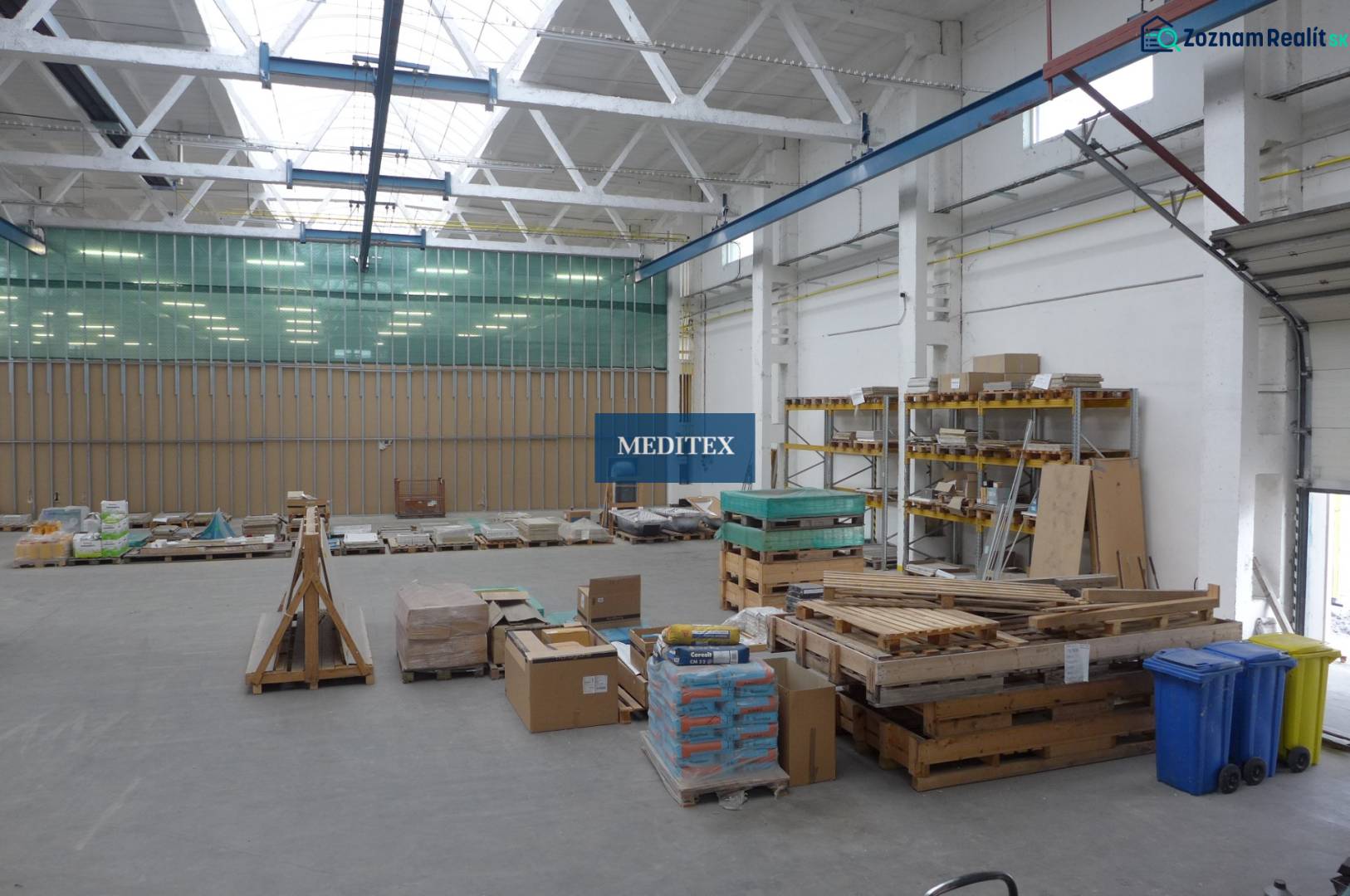 A raktárban raklapok vannak építőanyaggal és polcok táblákkal.