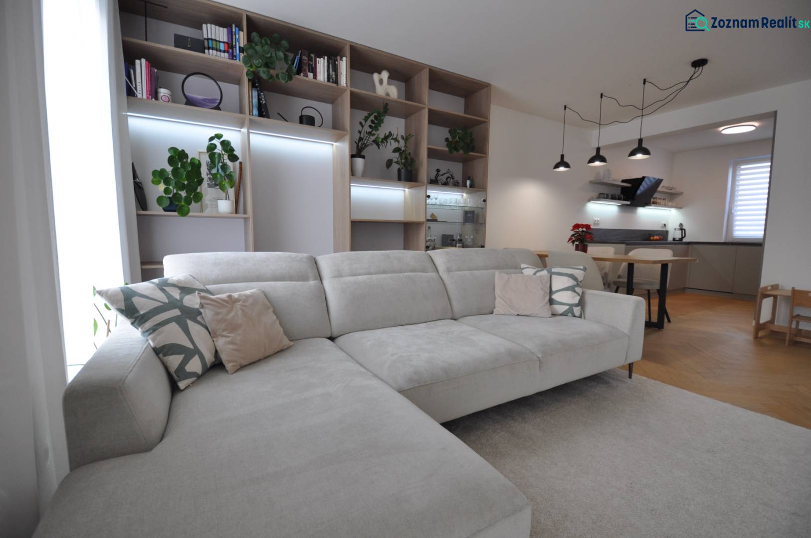 Nappali nagy kanapéval, könyvespolccal és konyhasarokkal egy családi házban.