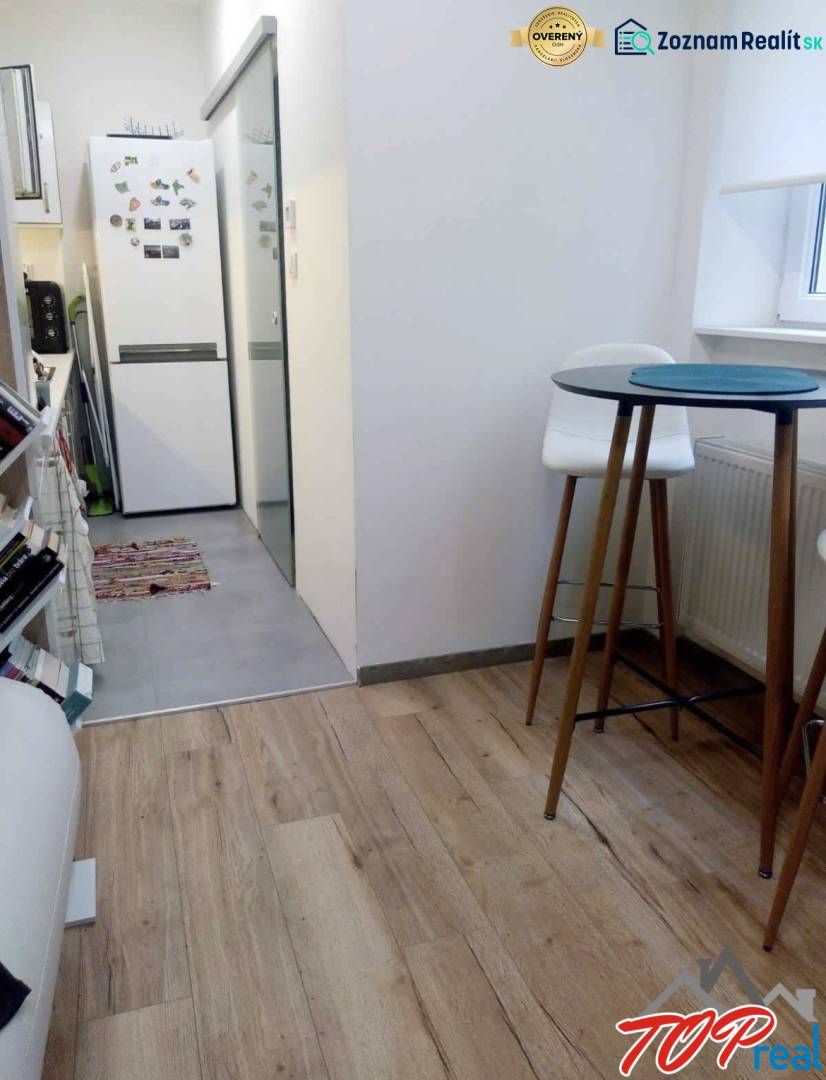 Konyha egy egyszobás lakásban fa dekorációjú padlóval, magas asztallal és székekkel.