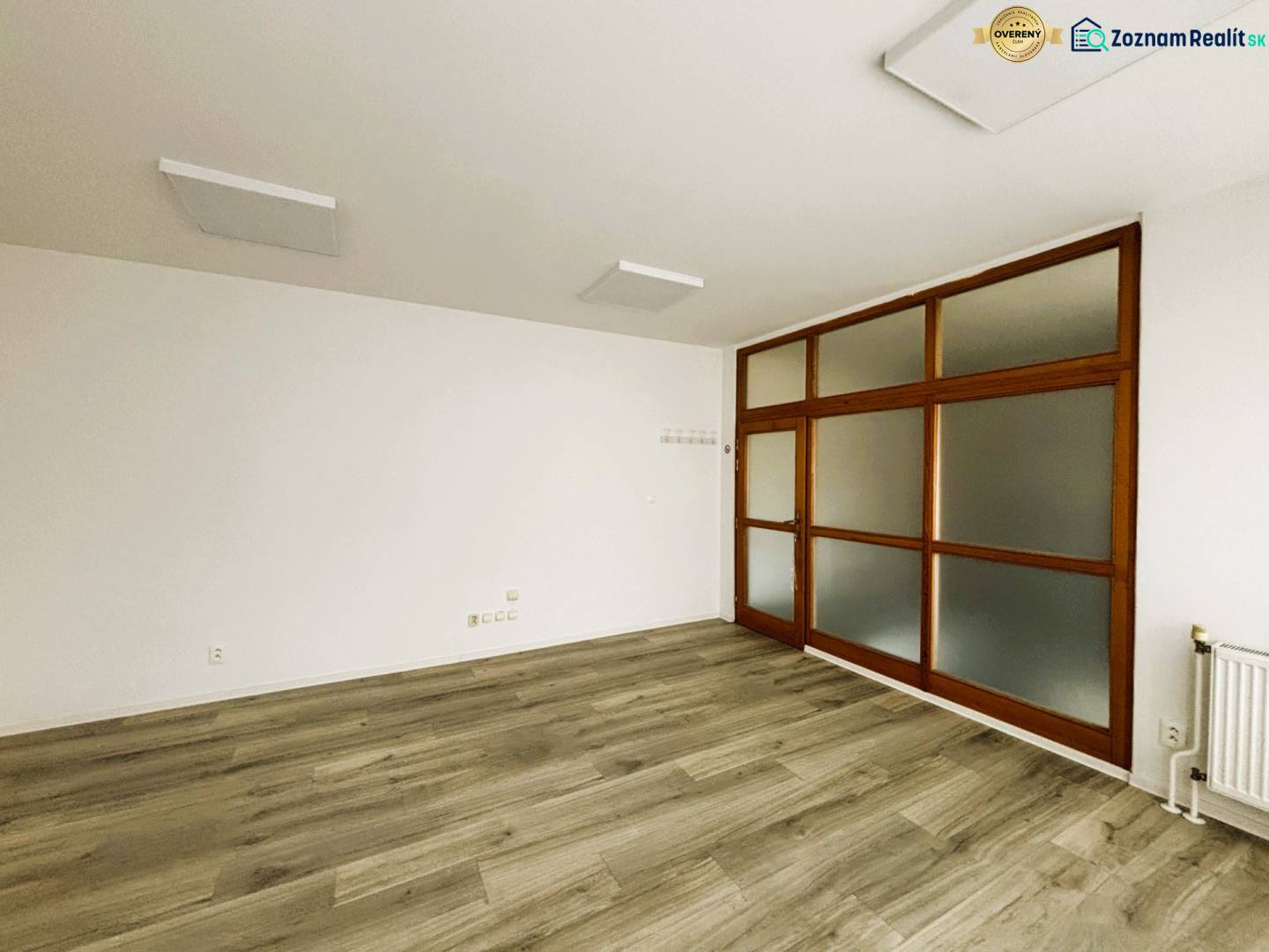 Kereskedelmi helyiségek fehér falakkal és fa dekoros padlóval, üvegajtókkal.