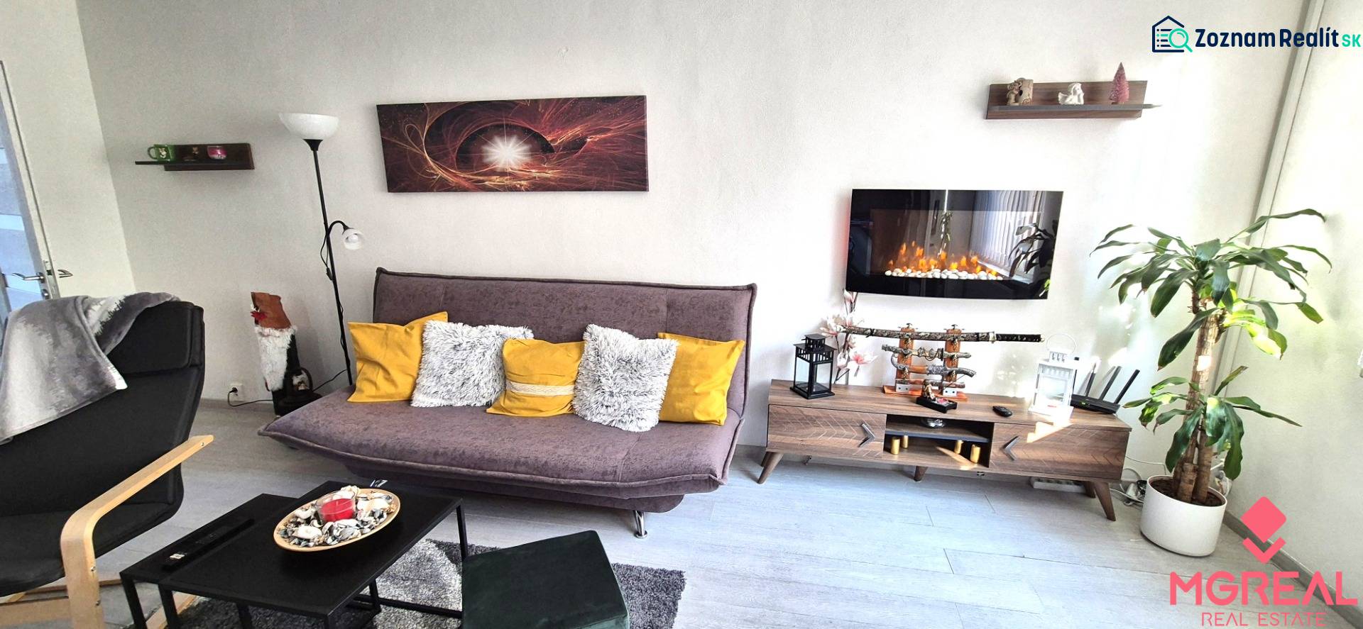 Nappali egy kétszobás lakásban kanapéval, polccal és elektromos kandallóval.