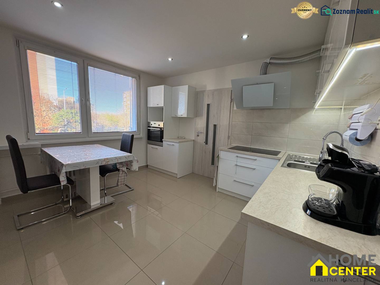 A háromszobás lakás konyhája nagy ablakokkal, étkezőasztallal és világos padlóval.