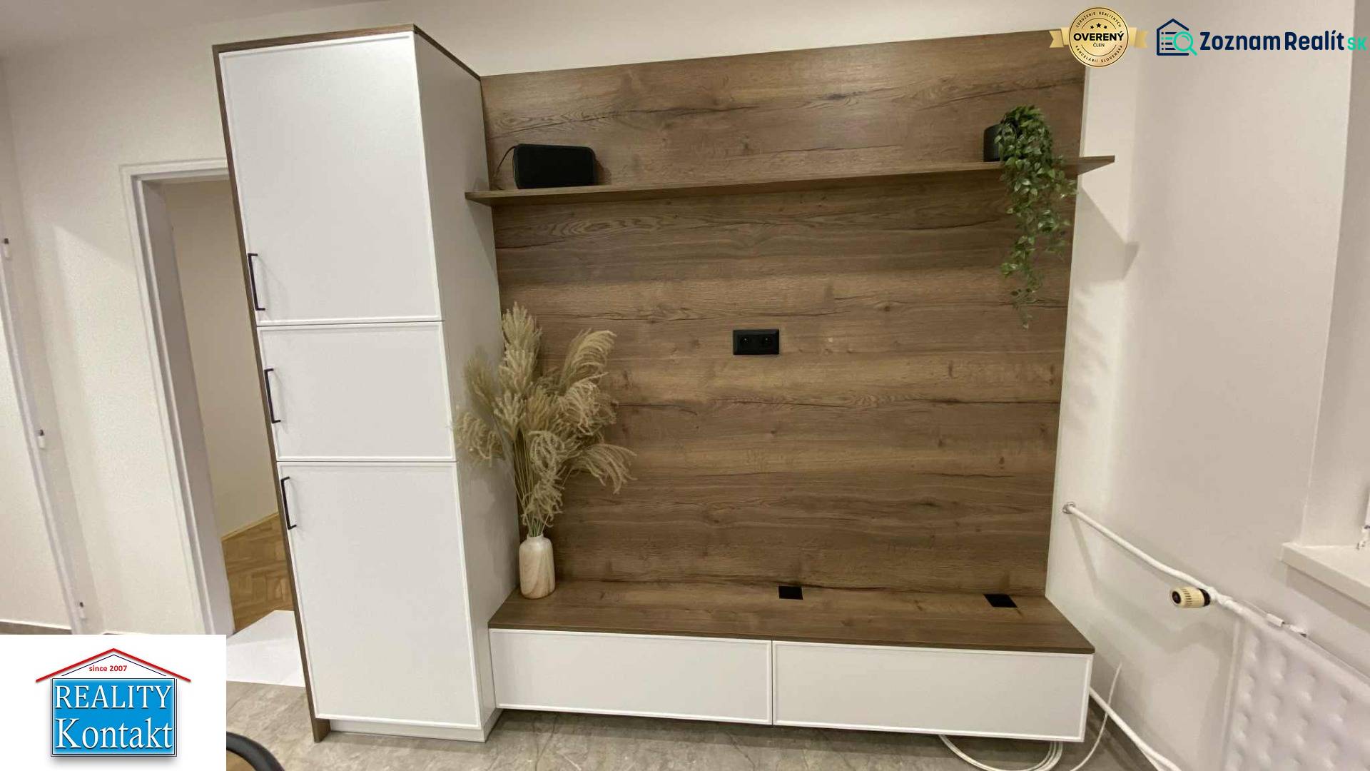 Az egyszobás lakásban van egy fa dekorációjú gardróbszekrény és egy váza virágokkal.