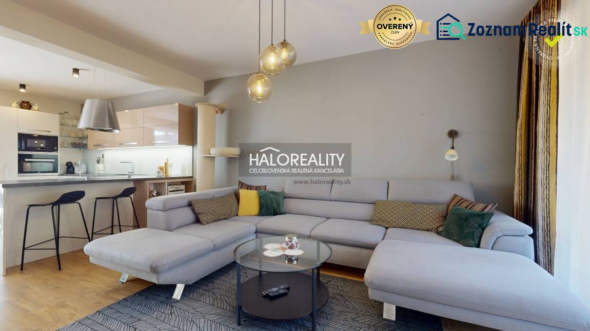 Tágas nappali egy családi házban kanapéval, konyhasarokkal és fa dekorációjú padlóval.