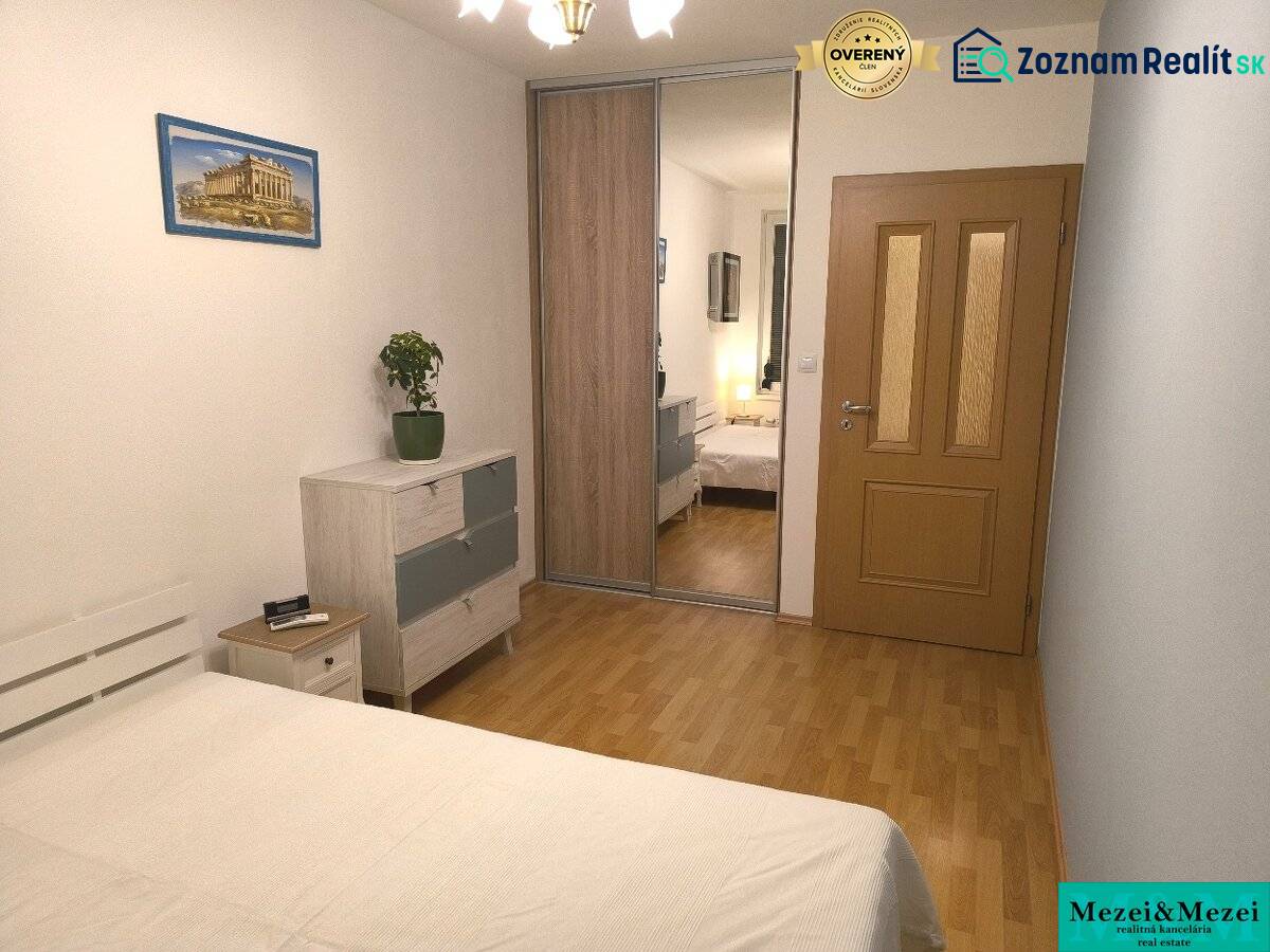 Hálószoba egy kétszobás lakásban fa dekor padlóval, tükrös szekrényekkel és képpel.