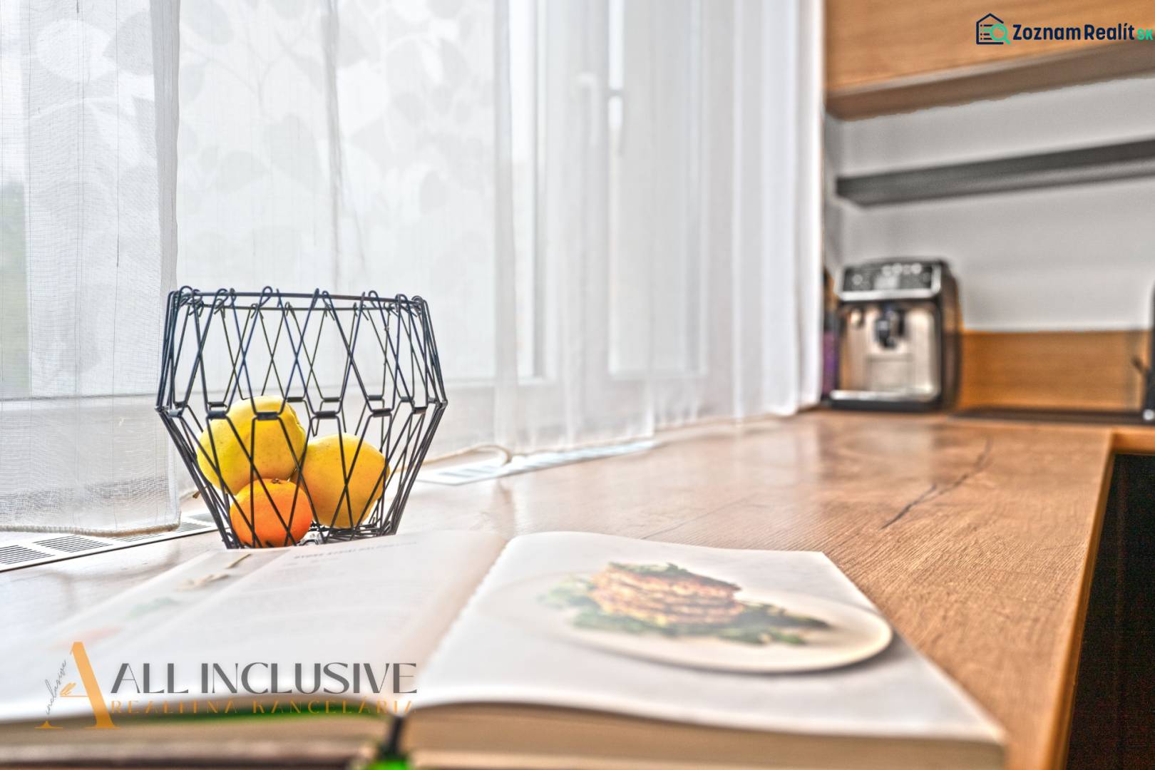 Nyitott konyha egy háromszobás lakásban fa dekorációval, gyümölcsöstál az asztalon.