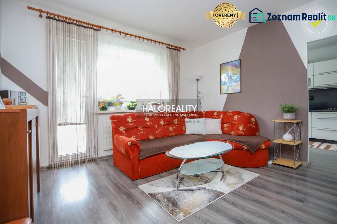 Nappali egy háromszobás lakásban narancssárga kanapéval és fa mintázatú padlóval.