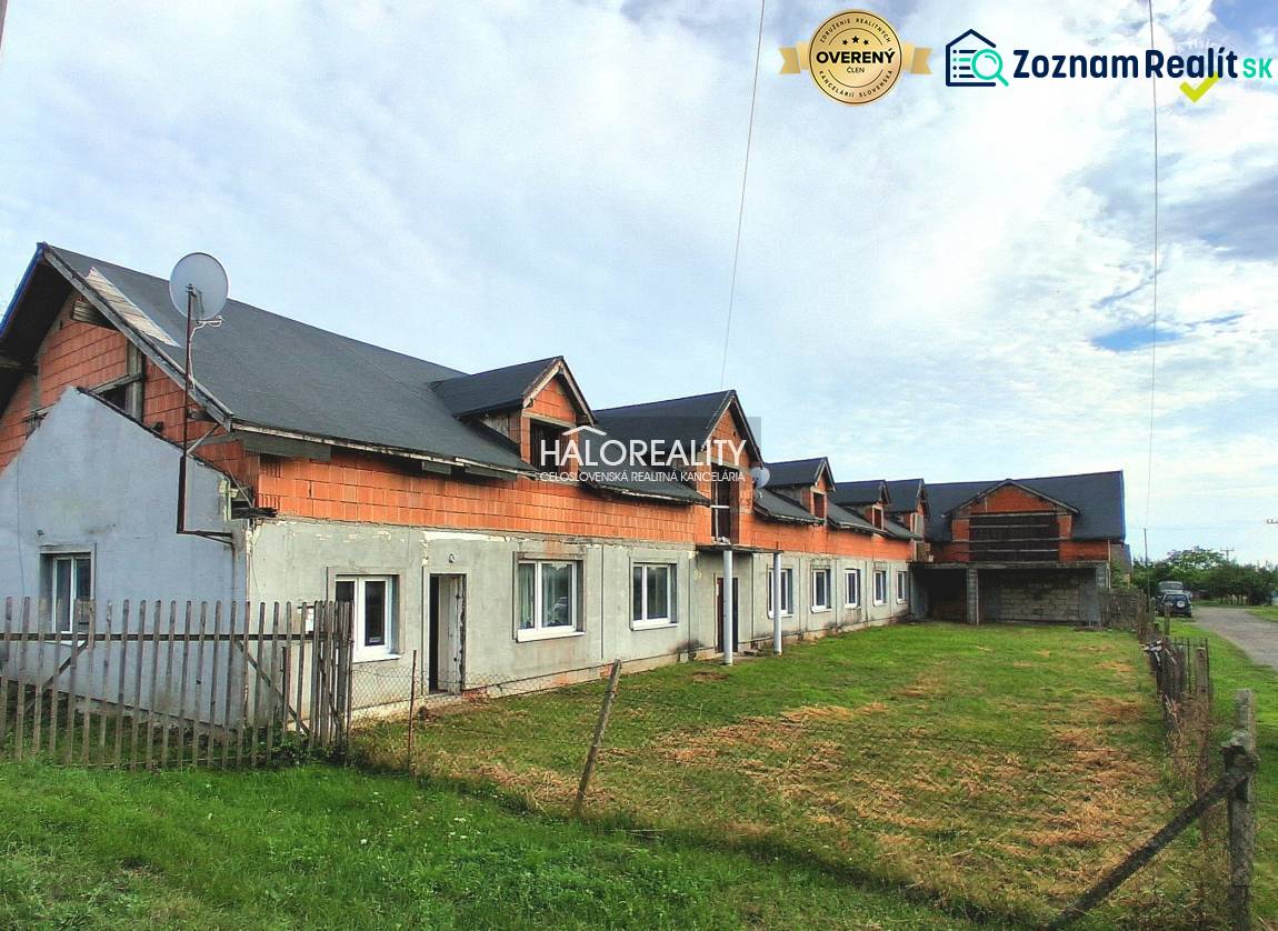 Üzlethelyiségek Tibaván, befejezetlen épület füves területtel és kerítéssel.