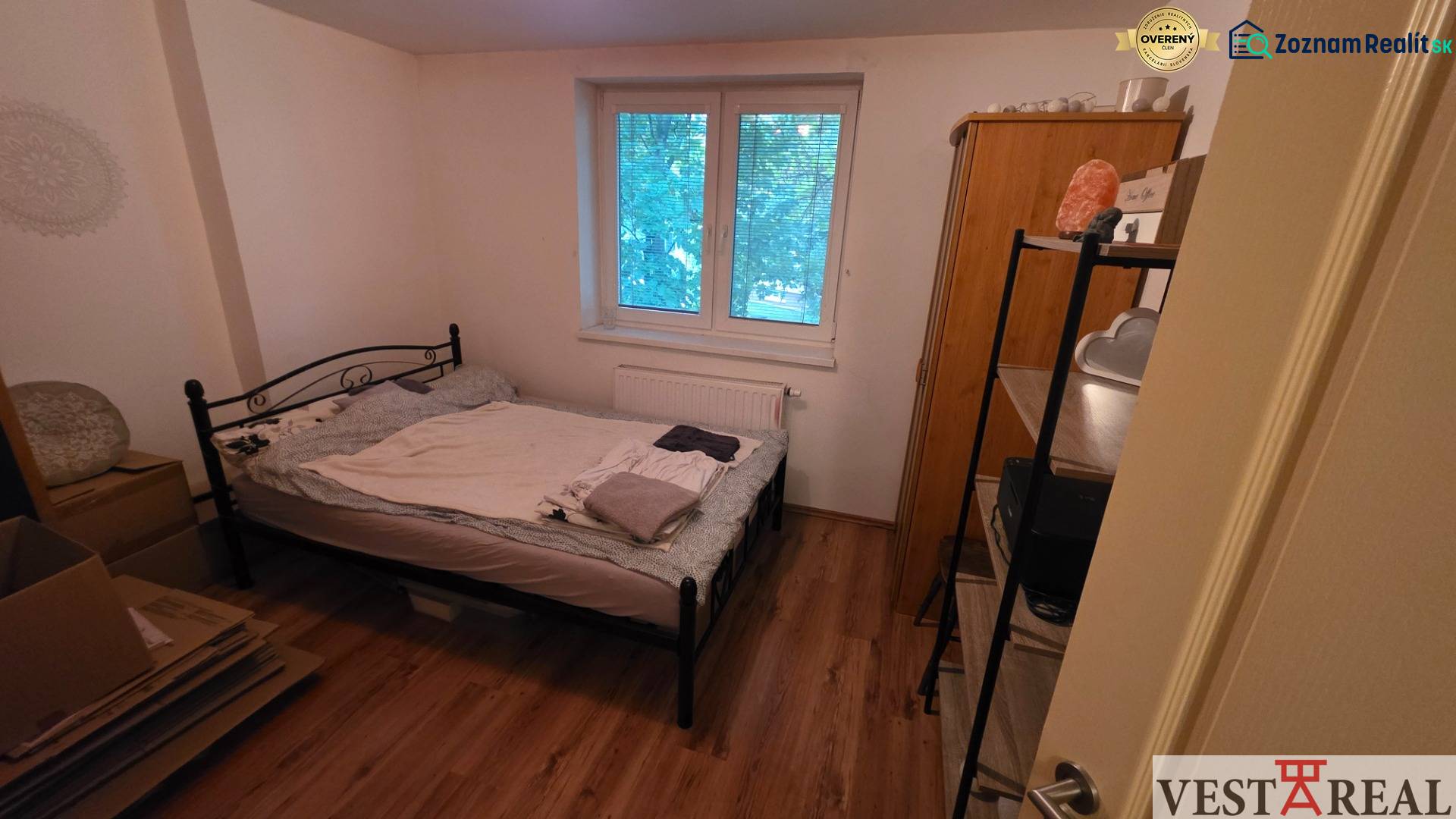 Hálószoba egy háromszobás lakásban fém ággyal és fa dekoros padlóval.