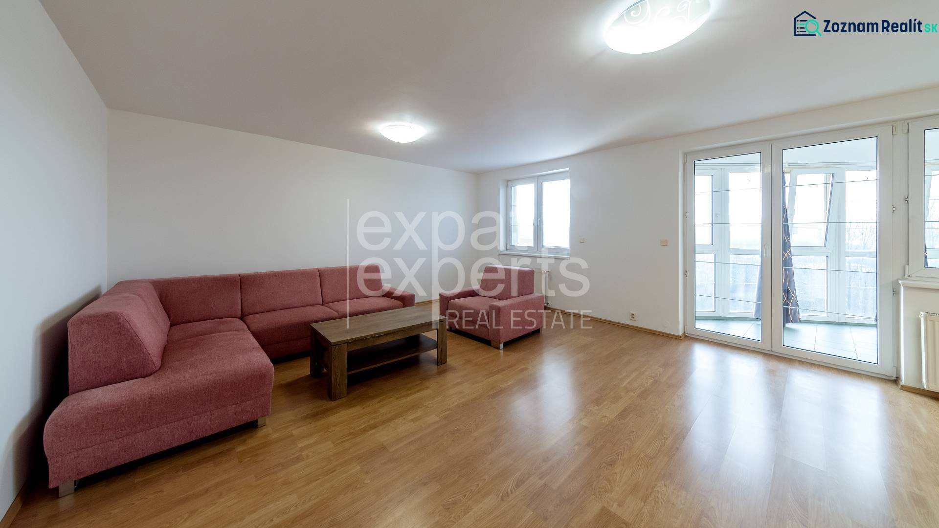 Nappali ülőgarnitúrával és fa mintázatú padlóval egy háromszobás lakásban.