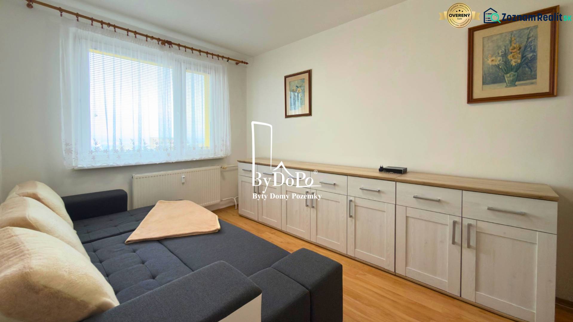 Szoba kanapéval, bútorokkal és fa dekorációjú padlóval egy háromszobás lakásban.