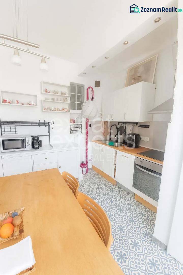 Konyha egy háromszobás lakásban étkezőasztallal, mintás padlóval és fehér szekrényekkel.