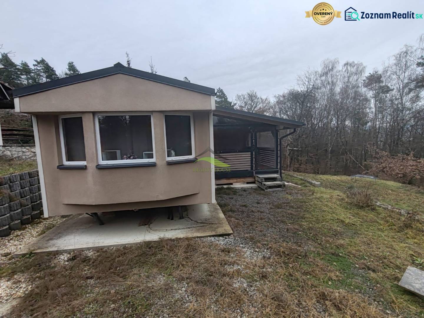 A Fő utcán található ház Újkelcsén, fákkal körülvéve és enyhén lejtős terepen.