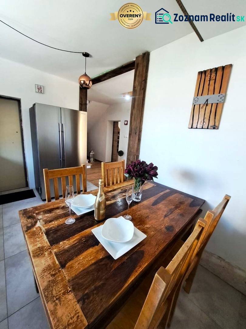 Családi ház konyhájában étkezőasztal kiegészítőkkel és hűtőszekrény.