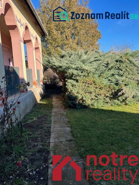 Családi ház Tomášovcén előkerttel és nagy fával a járda mellett.