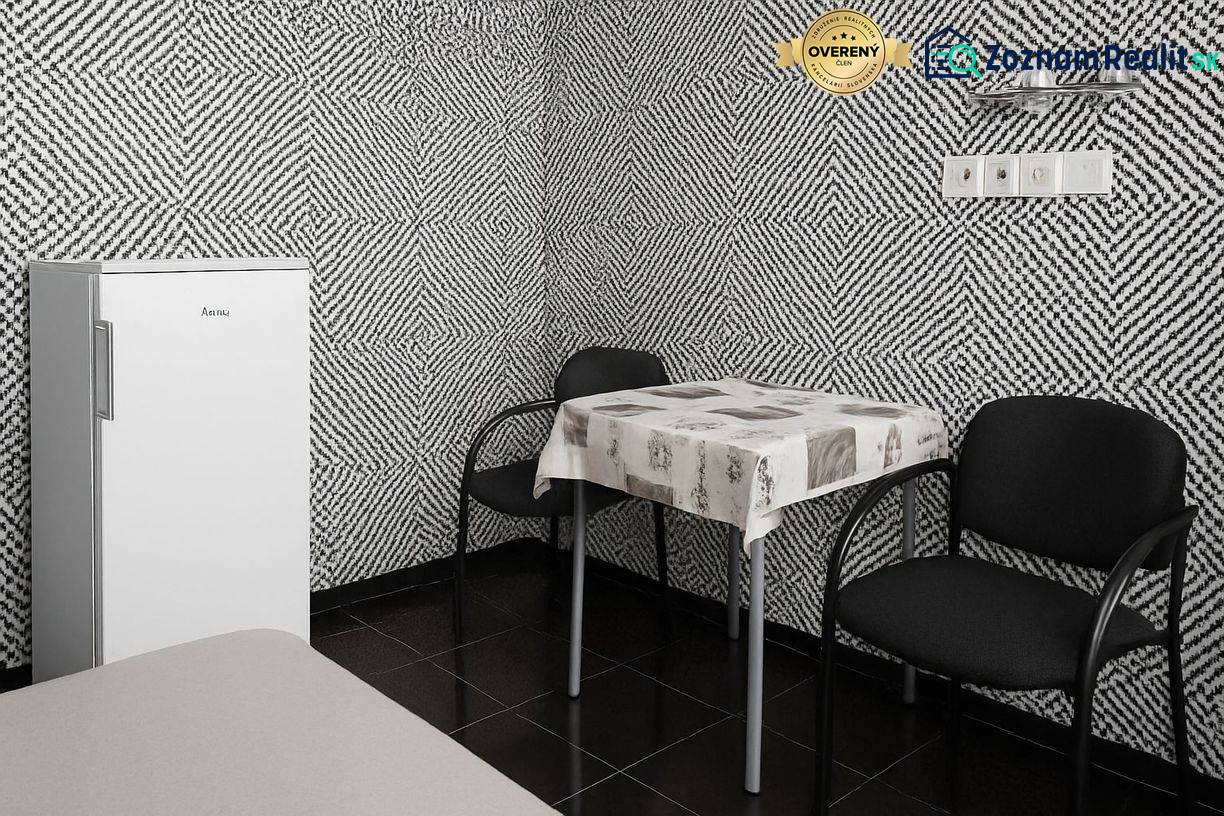 Belső tér fekete-fehér mintás tapétával, különálló hűtőszekrénnyel, asztallal és két székkel.