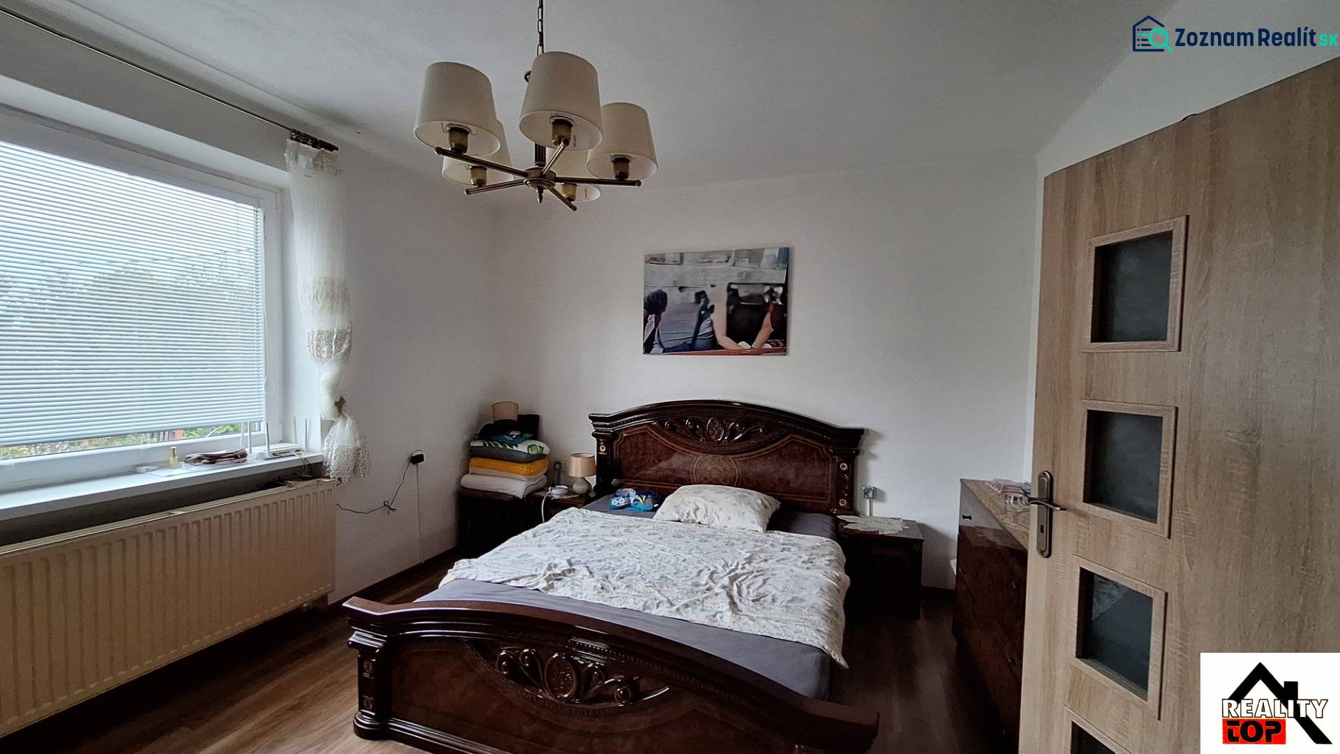 Hálószoba családi házban, ággyal, csillárral és fa dekorációjú padlóval.