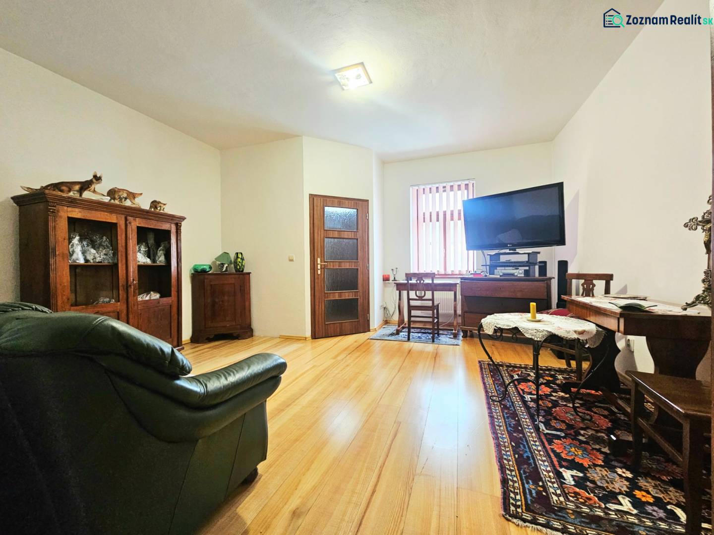 Nappali egy háromszobás lakásban, fa dekorációjú padlóval, kanapéval és televízióval felszerelve.