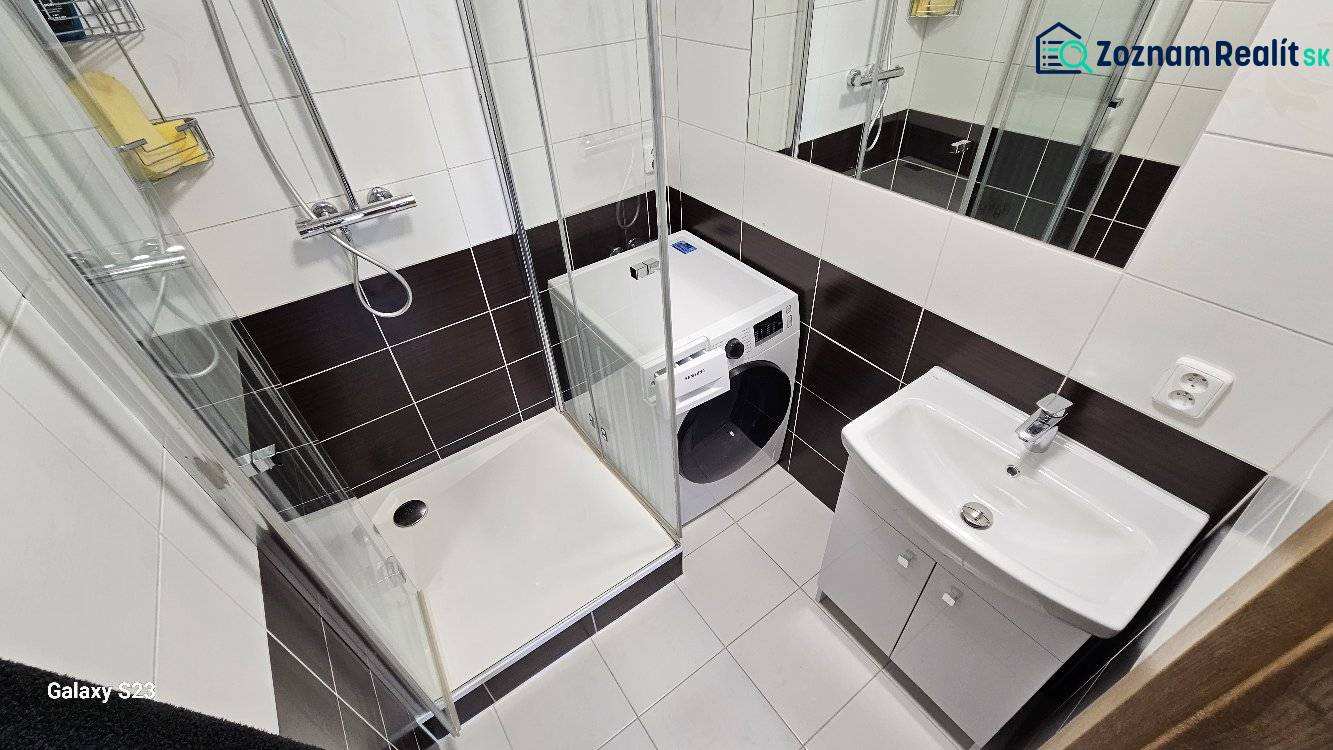 Fürdőszoba mosógéppel, zuhanyzóval és mosdóval egy háromszobás lakásban.