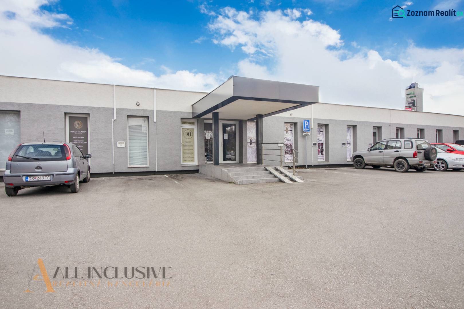 Egyszintes épület üzlethelyiségekkel a Vajanského utcán, parkolóval és autókkal a bejárat előtt.