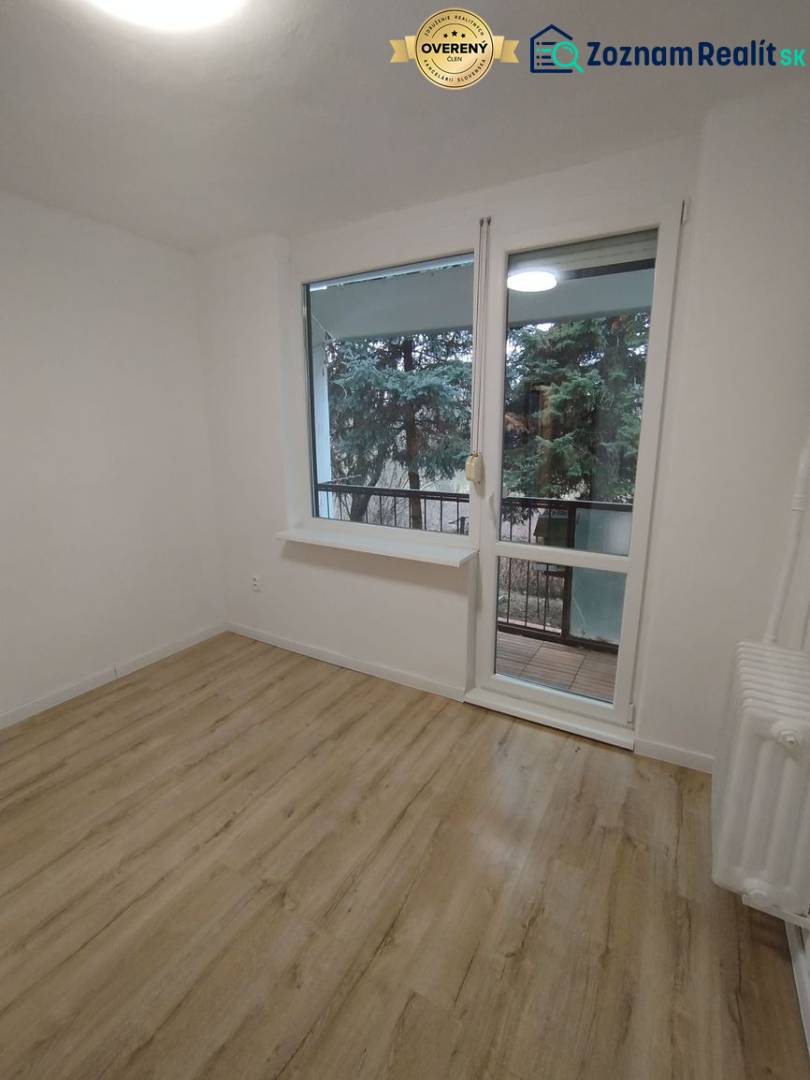 Szoba világos falakkal, fa mintázatú padlóval és kilátással a zöldre.