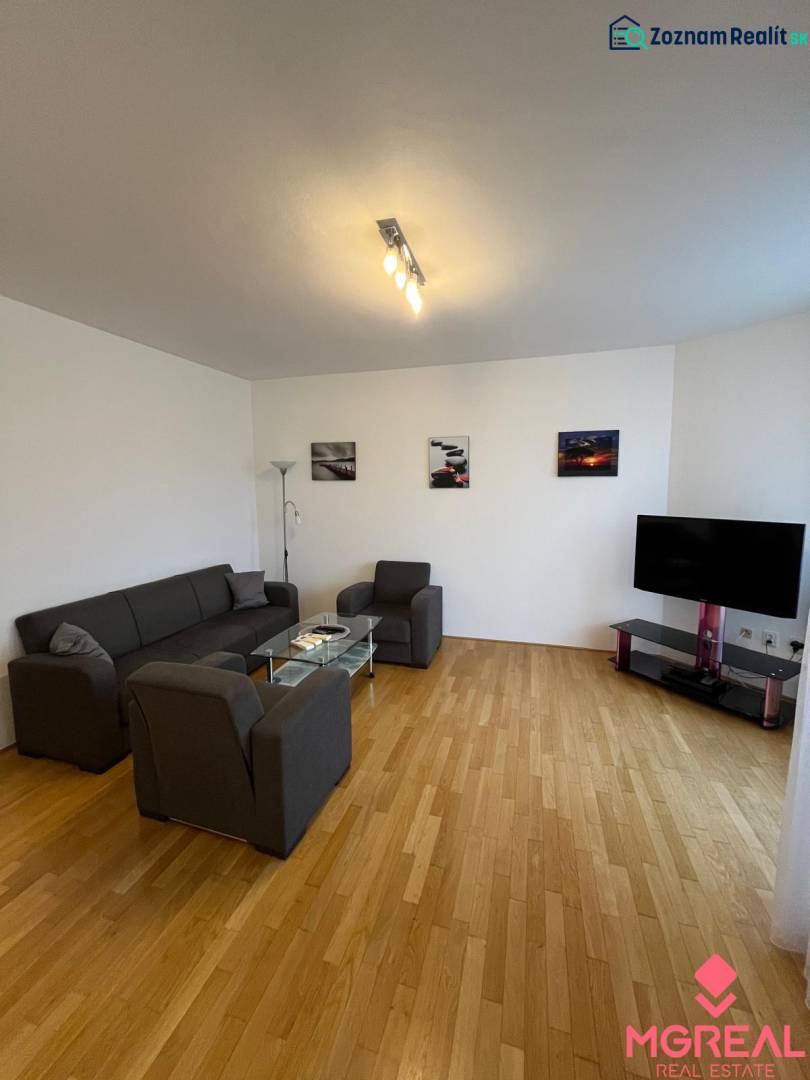 Nappali egy háromszobás lakásban, fa dekoros padlóval, kanapéval és televízióval.