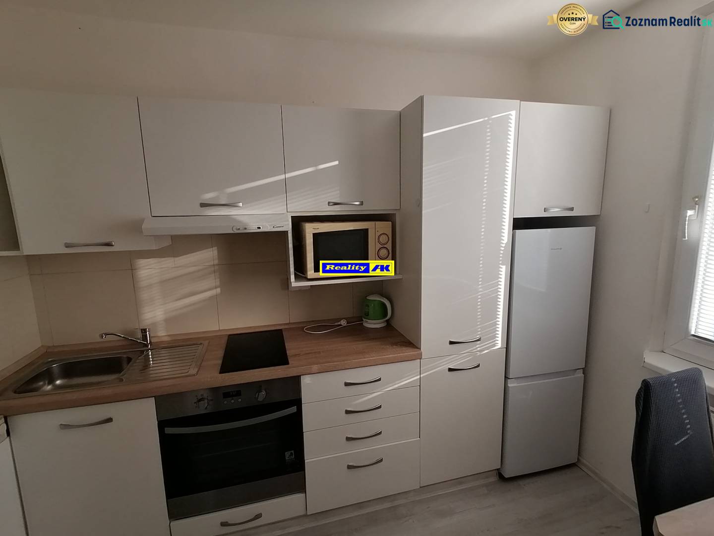 Konyha egy egyszobás lakásban, gépekkel és fehér bútorokkal.