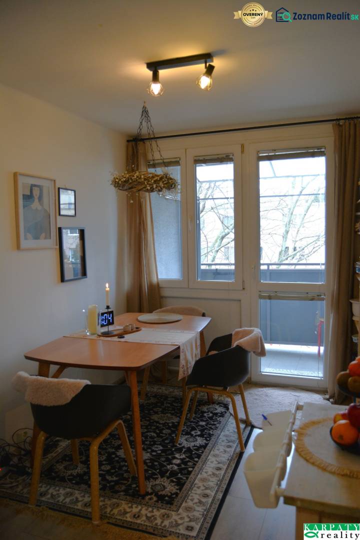 Étkező sarok egy háromszobás lakásban szőnyegmintával és üvegezett ajtókkal az erkélyre.