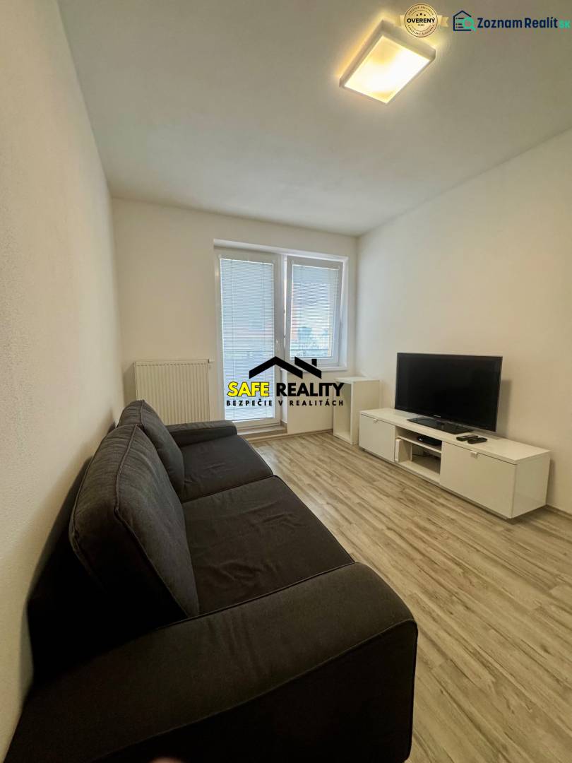 Nappali egy kétszobás lakásban kanapéval, televízióval és fa mintázatú padlóval.