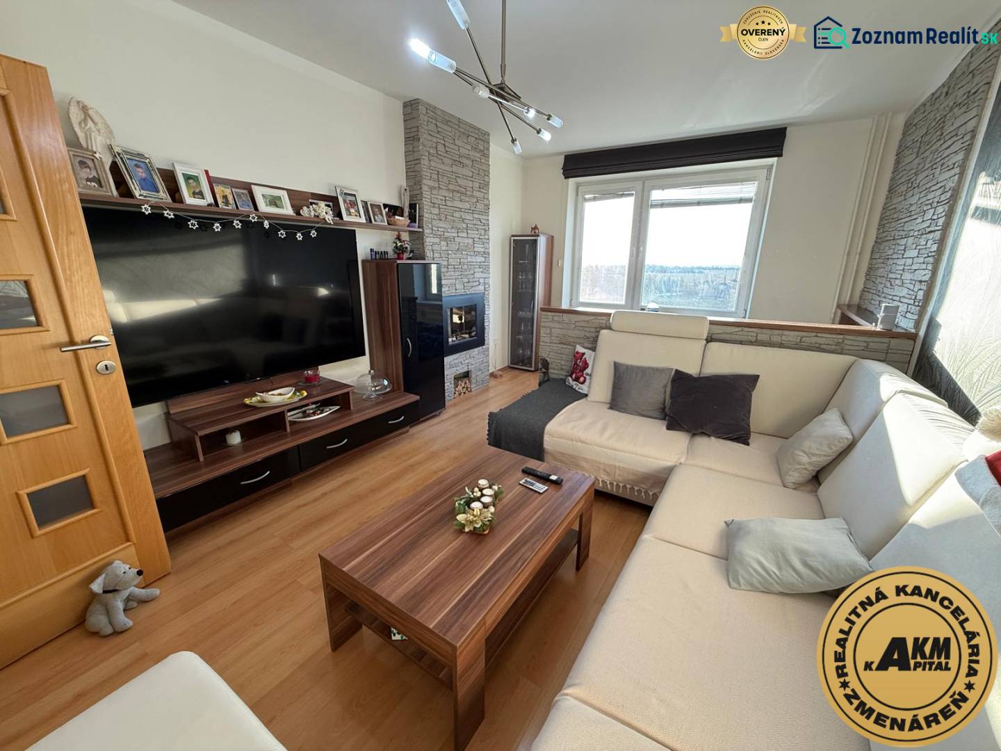 Nappali egy háromszobás lakásban kényelmes kanapéval, fa dekorációjú padlóval és televízióval.