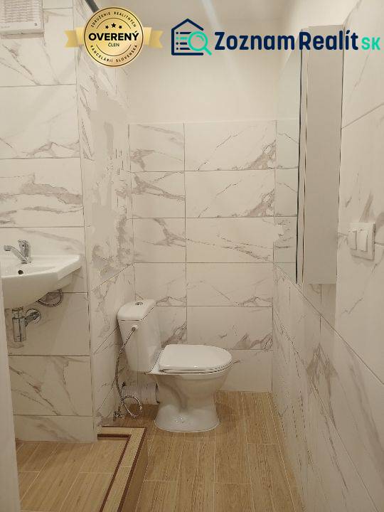 Garzonlakás fürdőszobája WC-vel, mosdóval és fa dekor padlóval.