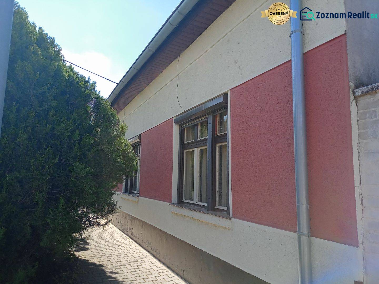 Családi ház Érsekújváron szigetelt homlokzattal és hálókkal, valamint fával a járda mellett.