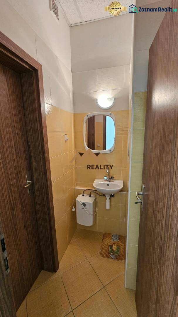 Egy kereskedelmi helyiségben található fürdőszoba mosdóval és tükörrel, világos csempékkel burkolva.