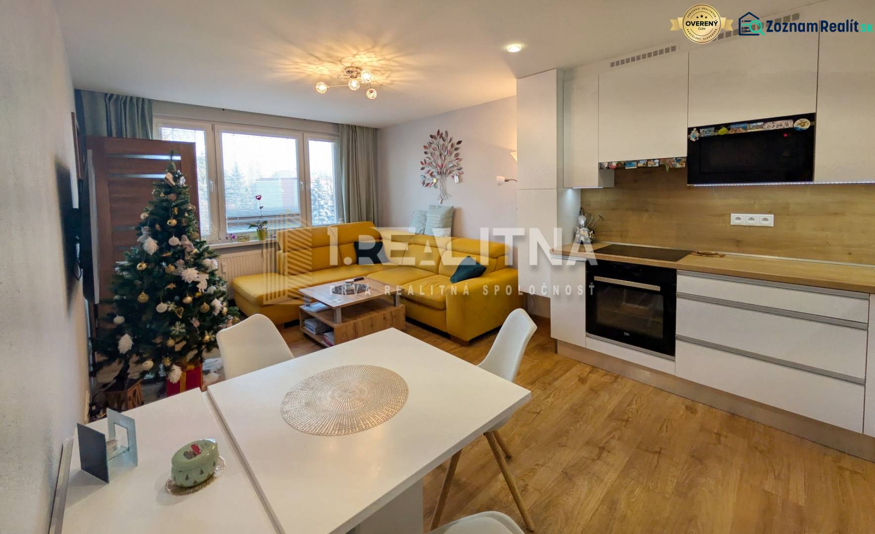 Nappali egy háromszobás lakásban fa dekor padlóval és konyhával.