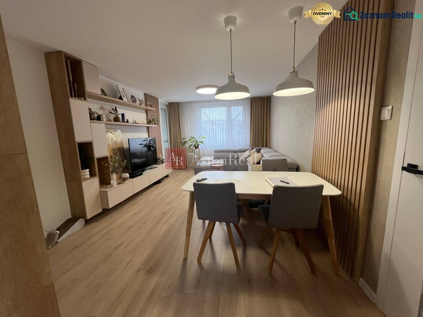 Nappali egy négy szobás lakásban kanapéval, TV-vel, étkezőasztallal és fa dekorációjú padlóval.