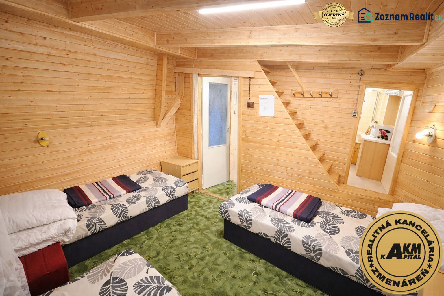 A ház belsejében két ágy, fa burkolatok és zöld szőnyeg található.