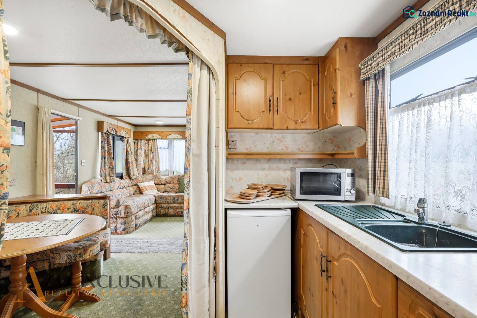 A faház belsejében konyha háztartási gépekkel és nappali virágos függönyökkel.