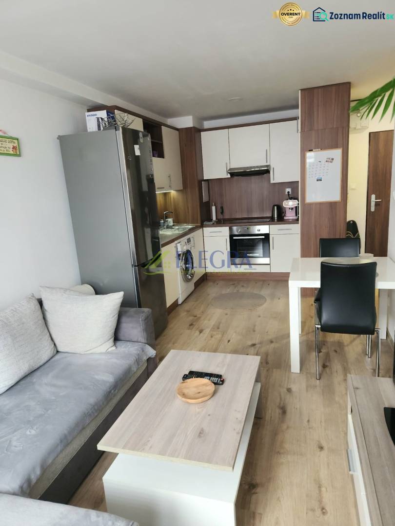 Nappali konyhasarokkal, kanapéval és fa dekorációjú padlóval egy kétszobás lakásban.