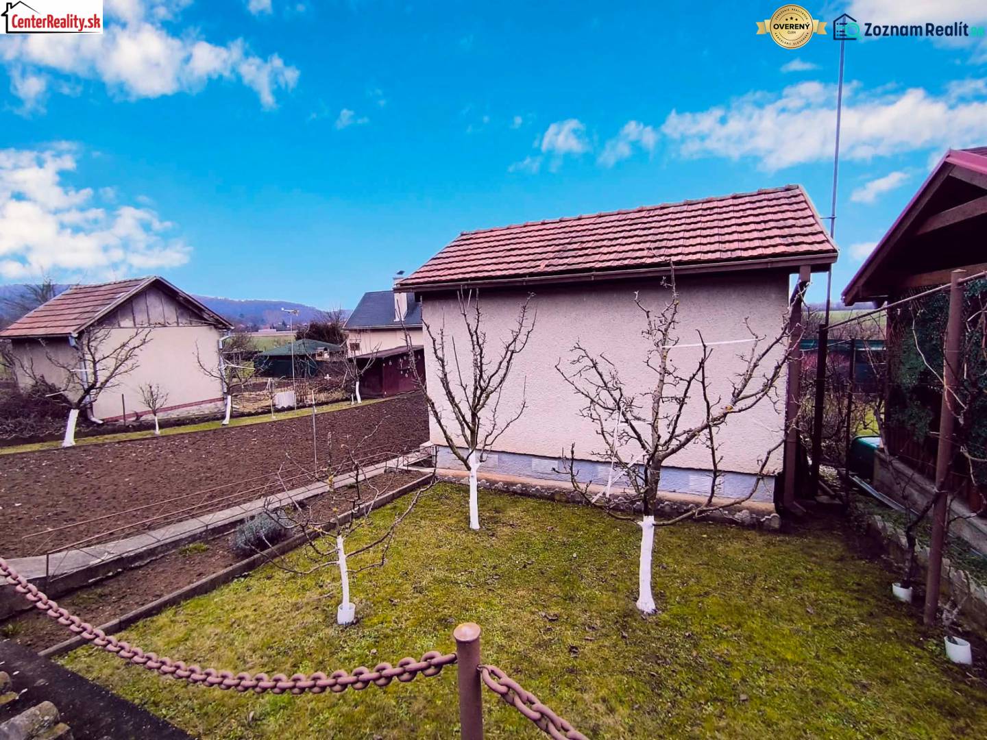 Kert házzal Partizánske városában, gyümölcsfák és megművelt föld, tiszta égbolt.