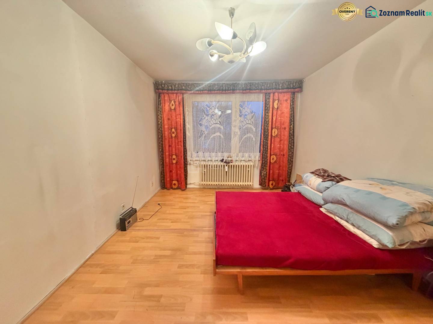 Hálószoba egy háromszobás lakásban ággyal, fa dekorációjú padlóval és világítással.